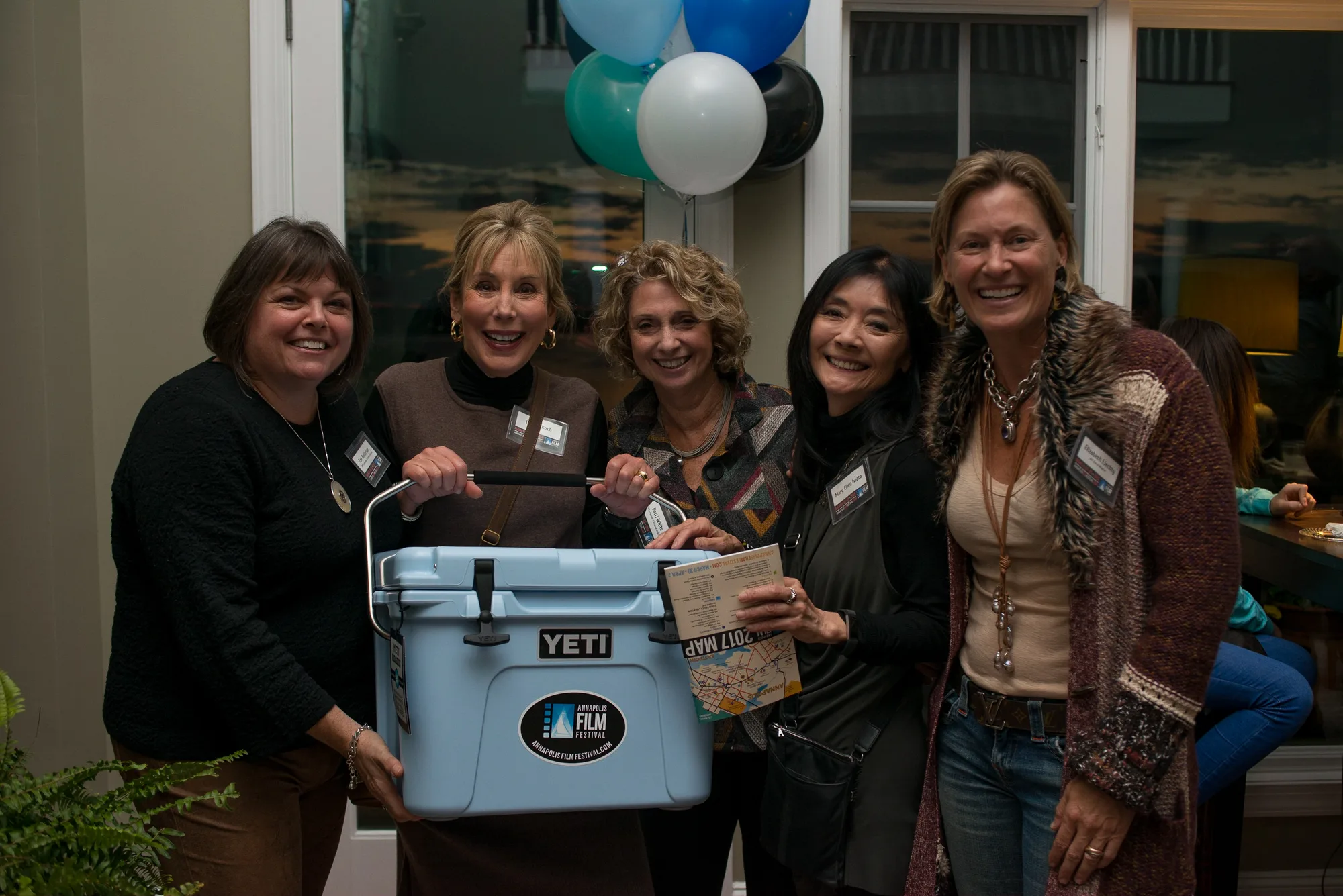 Five guests at a sponsorship event holding a branded cooler, balloons in the background.