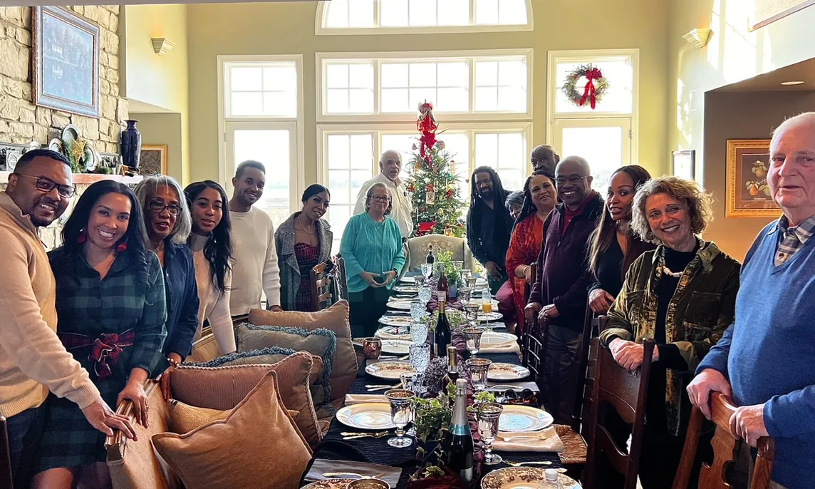 A long holiday dinner table with family and friends gathered around it.